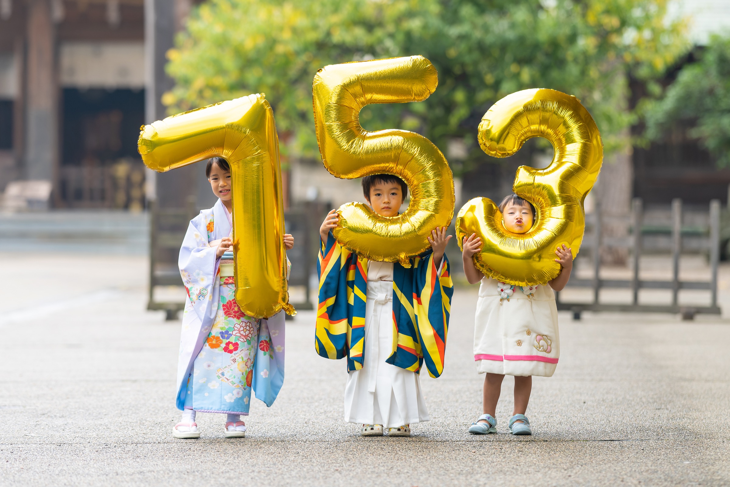 七五三の晴れ着で金色の数字バルーンを持つ三人きょうだい
