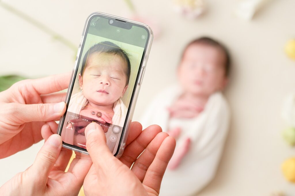 飯田市のニューボーンフォト出張撮影｜スマートフォンで赤ちゃんを撮影するパパとママの様子の写真
