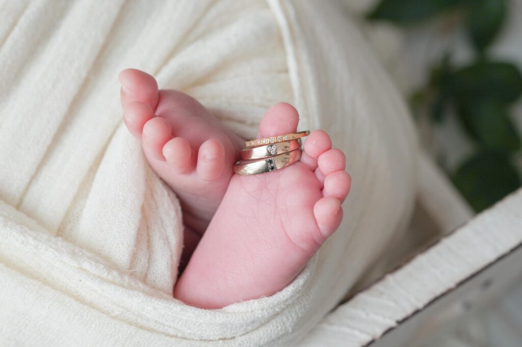 安曇野市でのニューボーンフォト｜白いおくるみの赤ちゃんの足にパパとママの結婚指輪と婚約指輪の写真