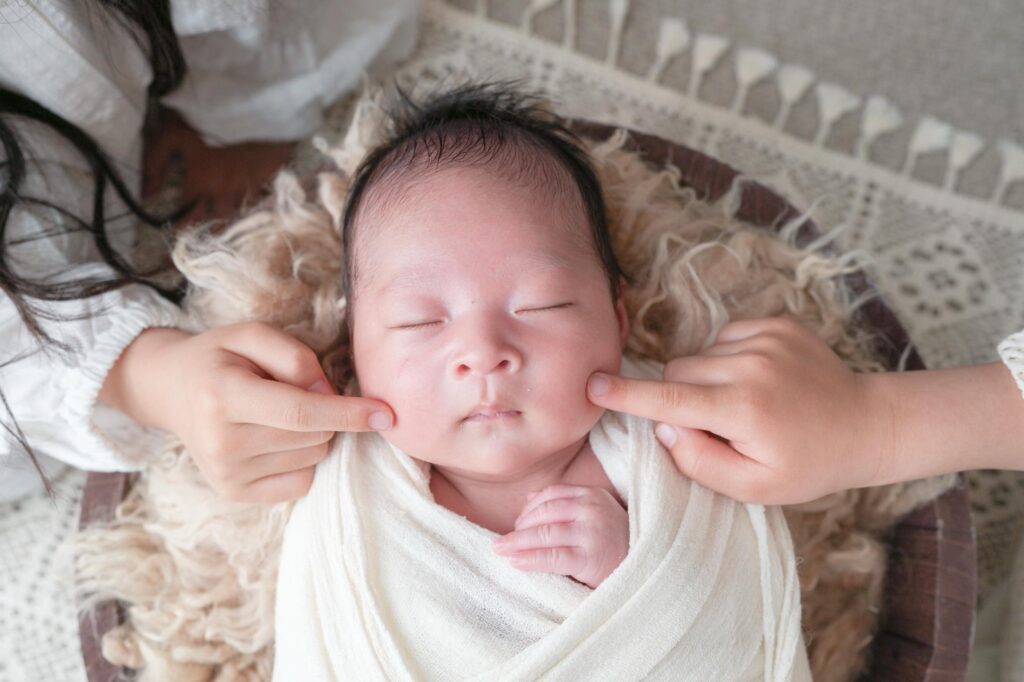 安曇野市でのニューボーンフォト｜お兄ちゃんとお姉ちゃんが赤ちゃんのほっぺたに触れているの写真