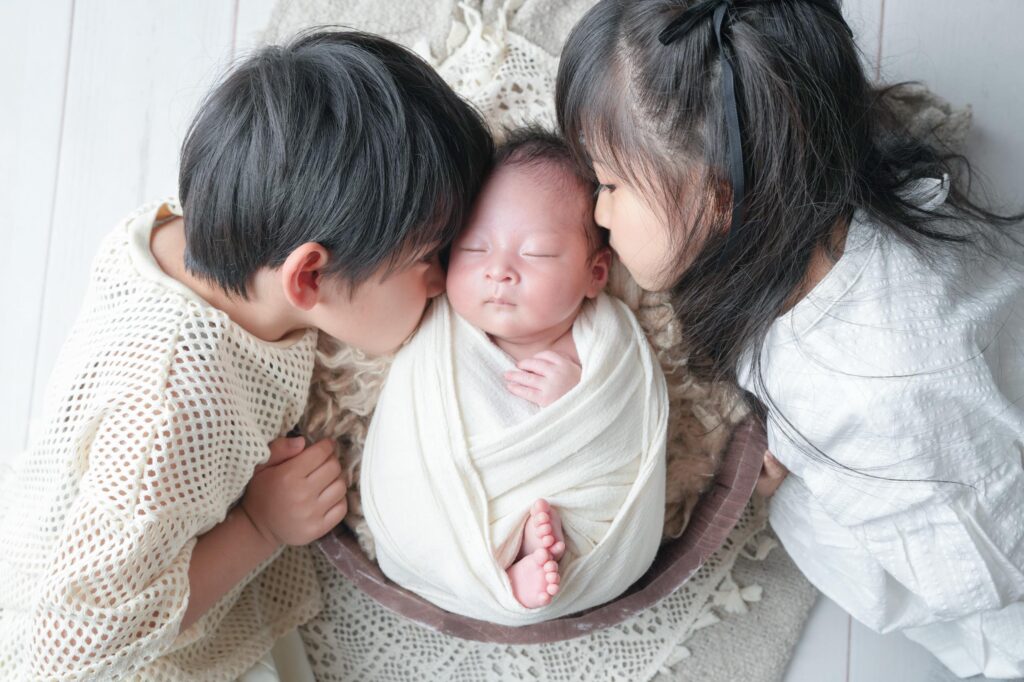 安曇野市でのニューボーンフォト｜お兄ちゃんとお姉ちゃんが赤ちゃんにキスをしているの写真