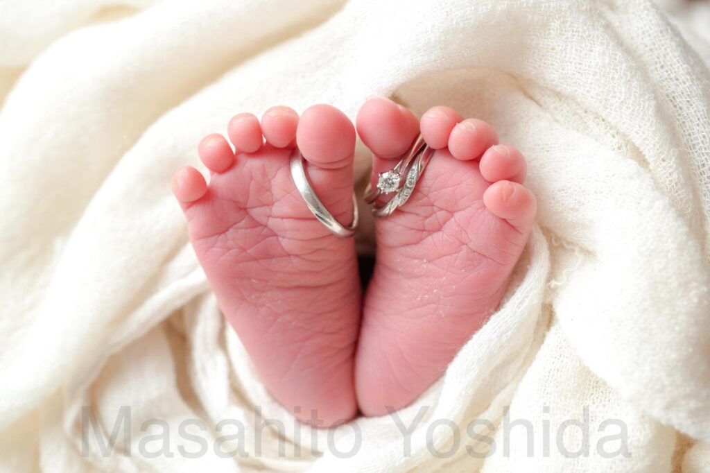 長野県大町市のニューボーンフォト｜白いガーゼに包まれた赤ちゃんの足に結婚指輪と婚約指輪をはめたディテール写真